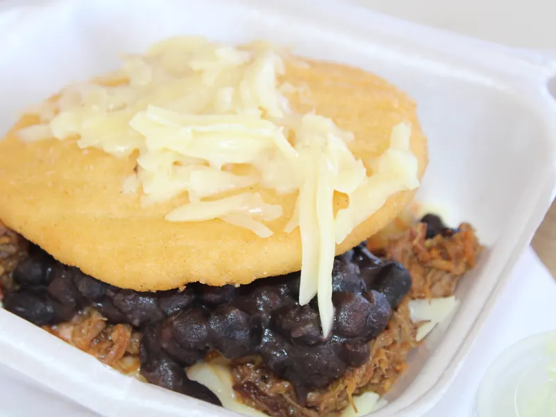 An arepa stuffed with shredded beef and black beans, topped with white cheese