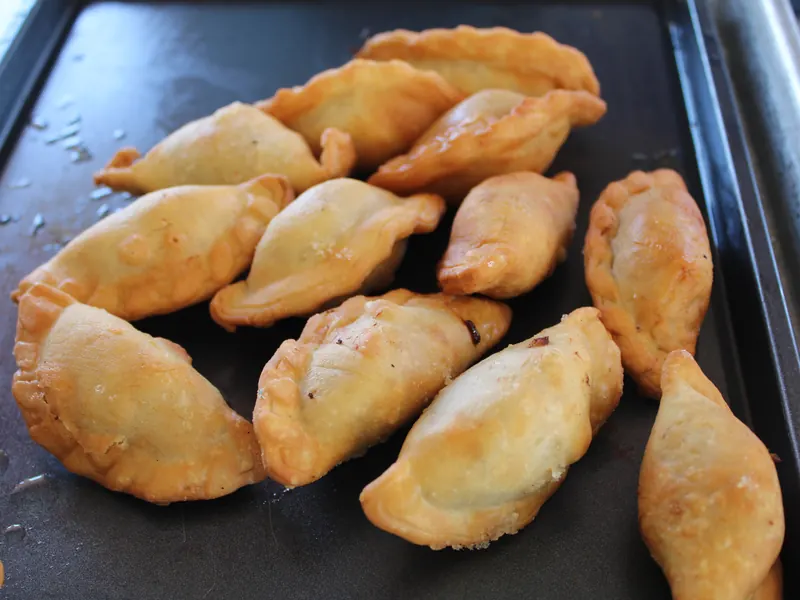 Golden empanadas lined up on a dark tray