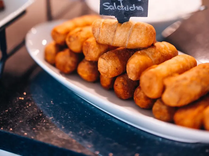 A platter of tequeños at a catered buffet, with a chalkboard sign